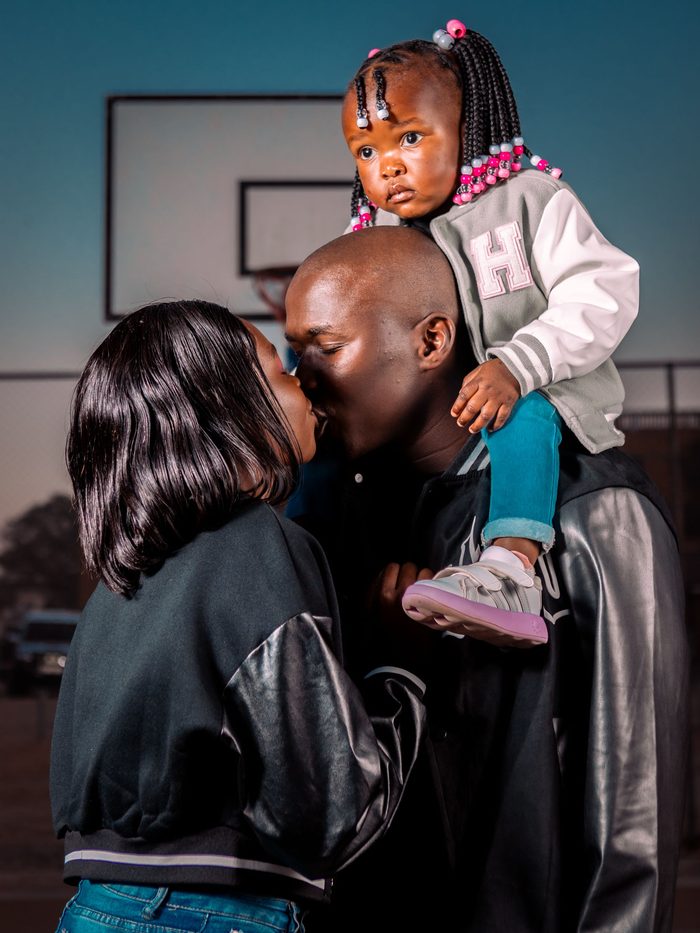 A family together outdoors, a young child carried on a parent's shoulder