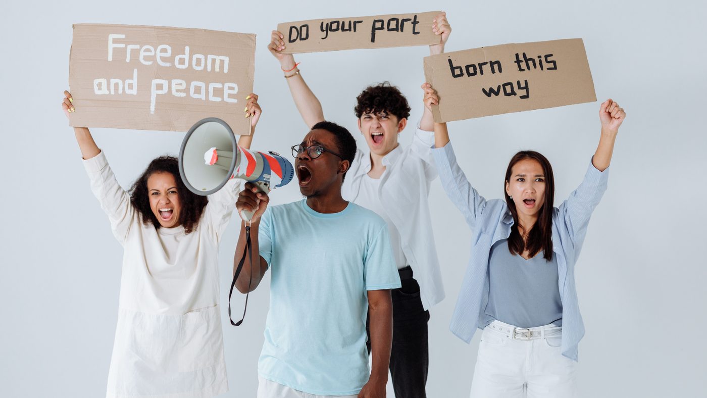 Four people with a megaphone holding signs reading Freedom and Peace, Do Your Part, and Born This Way