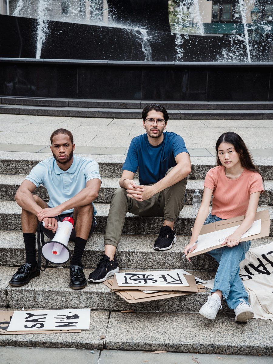 Three grassroots organizers sitting together on public steps with a megaphone and hand-made signs
