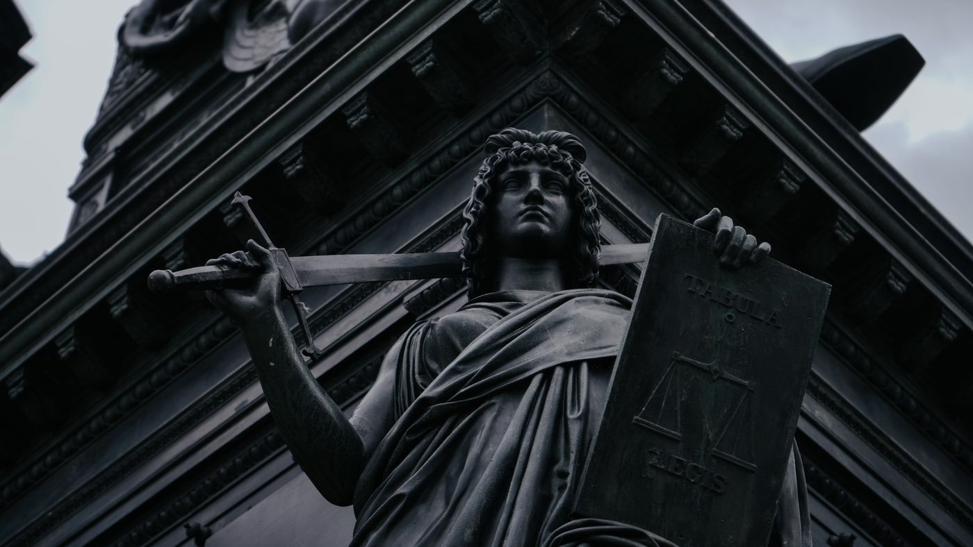 A bronze figure of Justice holding a sword and a tablet of law above a courthouse entrance