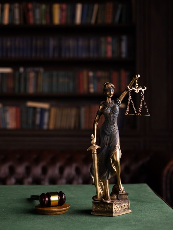 A figure of Justice holding scales beside a gavel on a desk in a law library