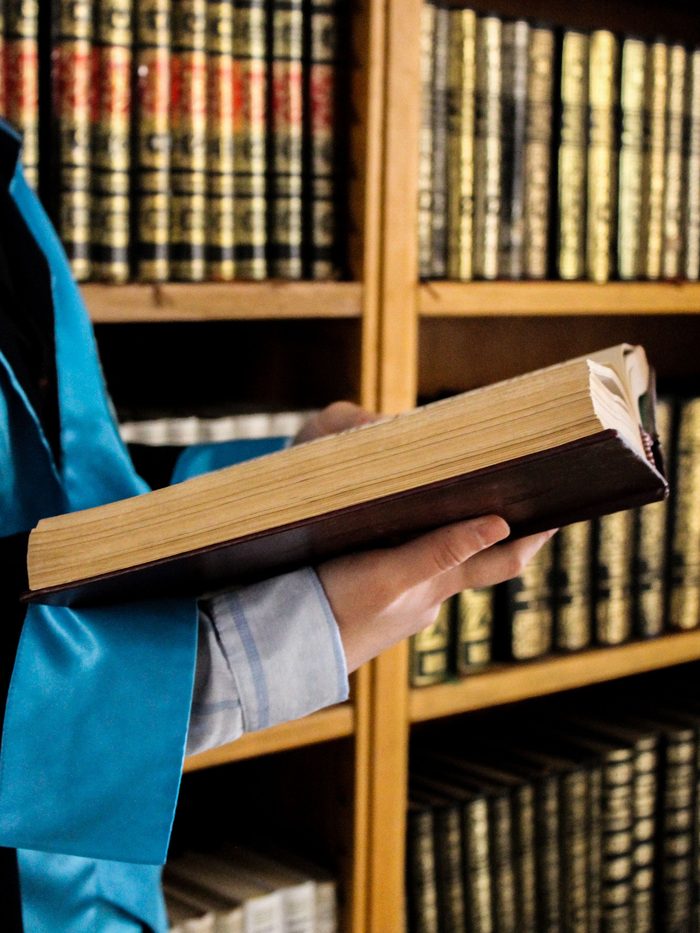 A person in robes holding a bound legal volume in front of library shelves