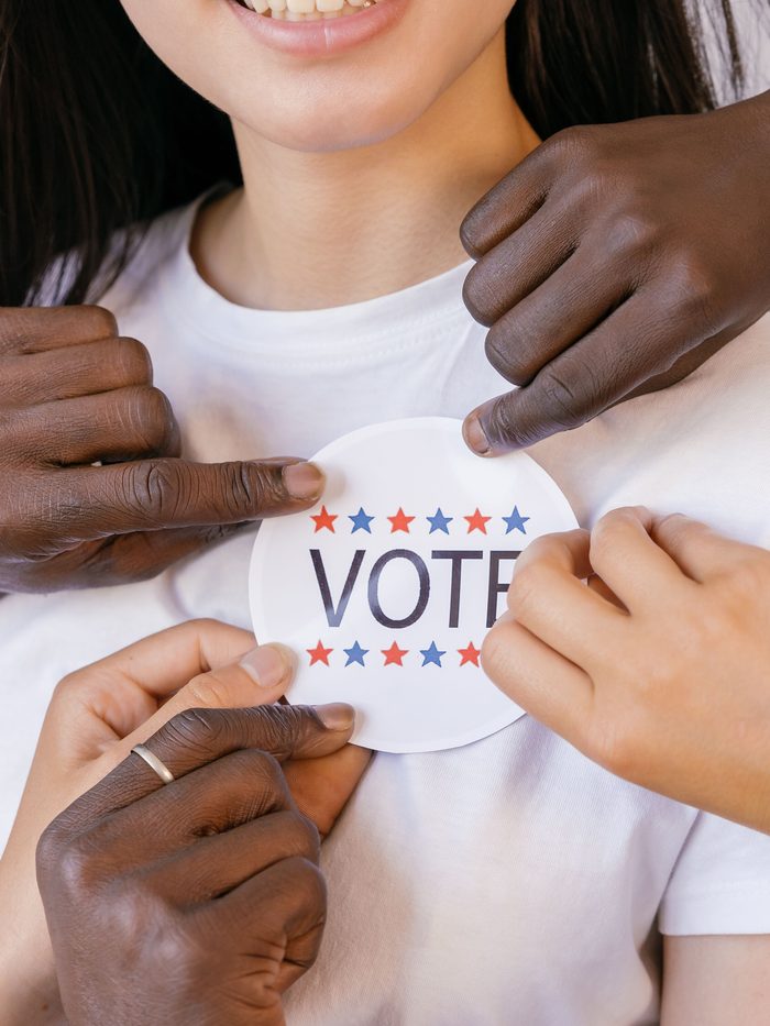 Several hands together placing a VOTE sticker on a person's shirt